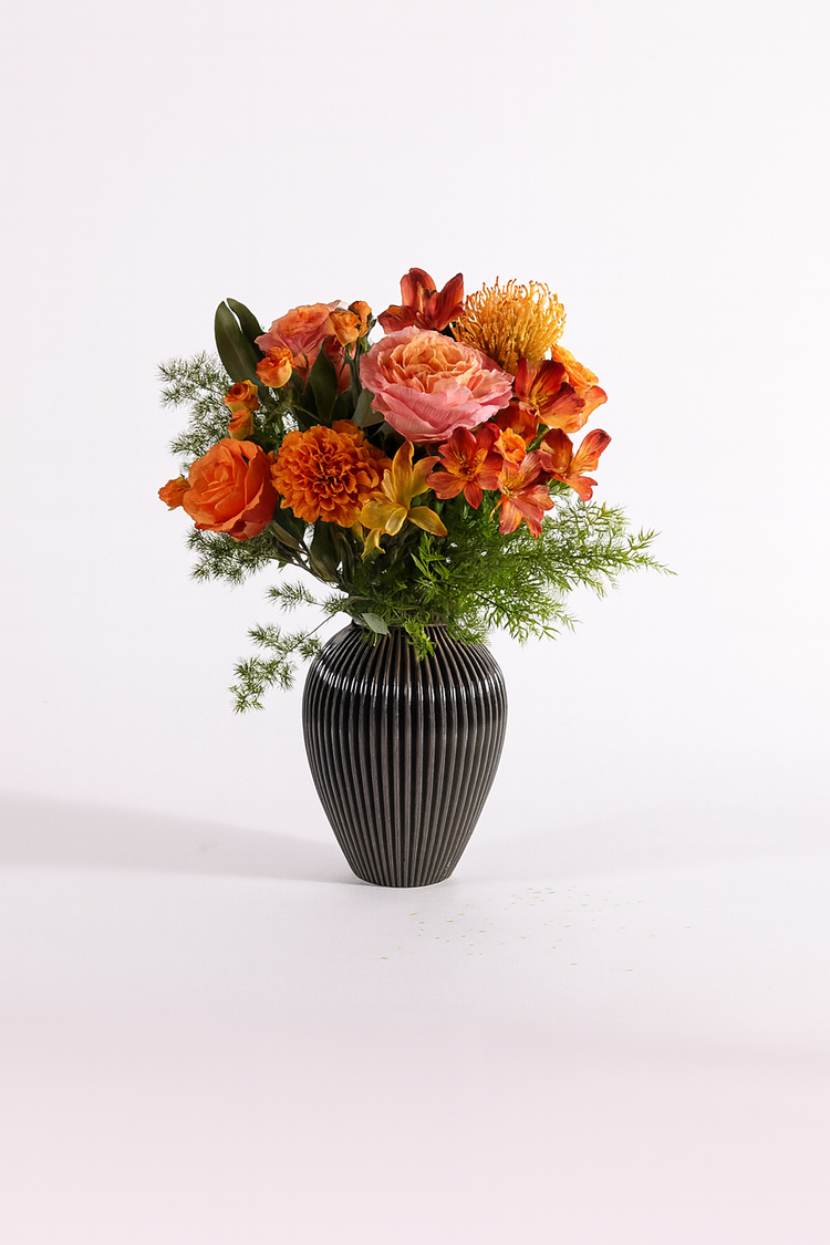 Bouquet autunnale nei toni arancio e rosa con rose e fiori stagionali in vaso nero