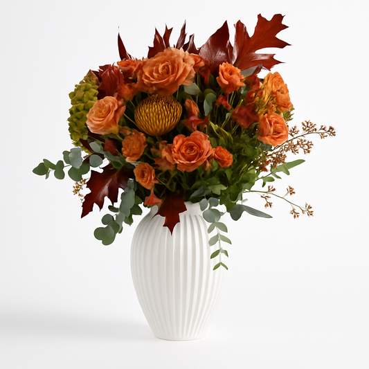 Composizione autunnale nei toni arancio e ruggine con rose, foglie decorative ed eucalipto in vaso bianco