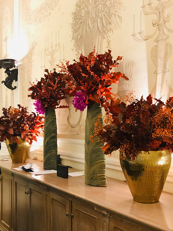 Allestimento floreale autunnale per concierge con foglie, bacche e fiori nei toni arancio e bordeaux